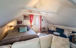 Ein gemütliches Schlafzimmer unter dem Dach mit Bett, Sofa, kleinem Tisch und einer Chandelier.
