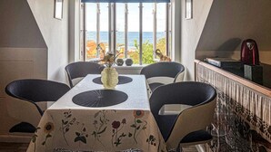 A dining area with a table, chairs, a vase, and a view of the sea through large windows. - 1 bedroom gorgeous apartment in Gudhjem (Gudhjem)