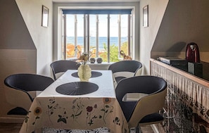 Ein Essbereich mit Tisch, Stühlen, einer Vase und Meerblick durch große Fenster.