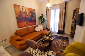 Uma sala de estar com sofá, mesa de centro, televisão e um quadro na parede.
