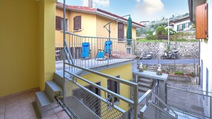 Een balkon met metalen hekwerk, een gele muur en uitzicht op een straat met geparkeerde scooters.
