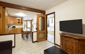 A room with a dining table, chairs, a TV, wooden cabinets, and a kitchen area. - 2 bedroom nice home in Monte Isola (Monte Isola)