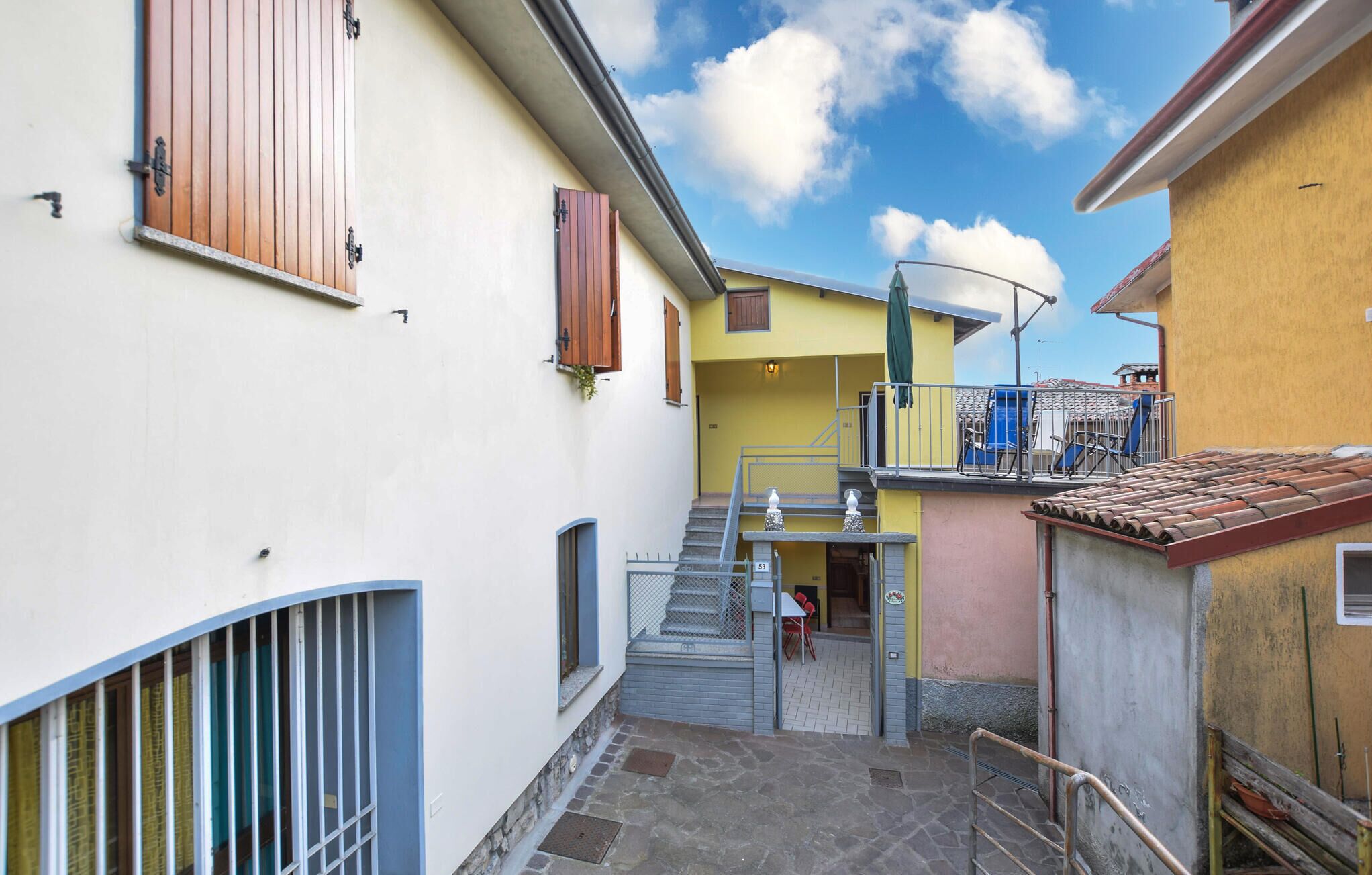 A narrow alleyway with a staircase leading to a yellow building, a metal gate, and a blue railing.