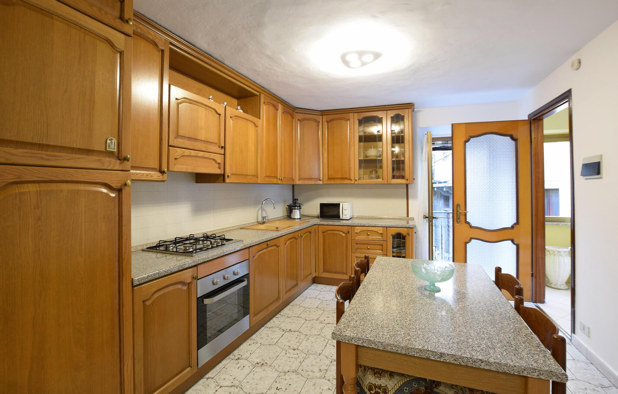 A kitchen with wooden cabinets, a granite countertop, a stove, an oven, a microwave, and a dining table with chairs.