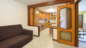 Een woonkamer met een bruine bank, een keuken met houten kasten en een magnetron, en een glazen deur die naar een andere kamer leidt.
