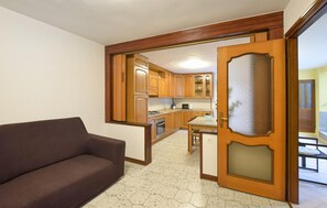 A living room with a brown sofa, a kitchen with wooden cabinets and a microwave, and a glass door leading to another room. - 2 bedroom nice home in Monte Isola (Monte Isola)