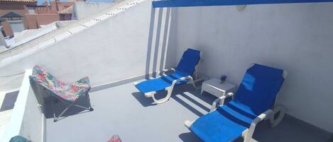 A rooftop terrace with blue lounge chairs, a small table, and a colorful chair.