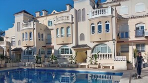 Zona de piscina amb una piscina blava cristal·lina, envoltada d'edificis amb balcons i finestres d'arc.