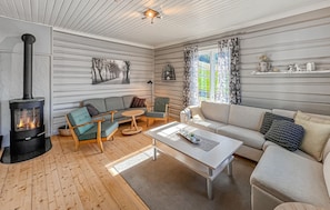 A cozy living room with a wood-burning stove, a sofa, a chair, a coffee table, and a window with curtains. - Gorgeous home in Svatsum with WiFi (Svatsum)