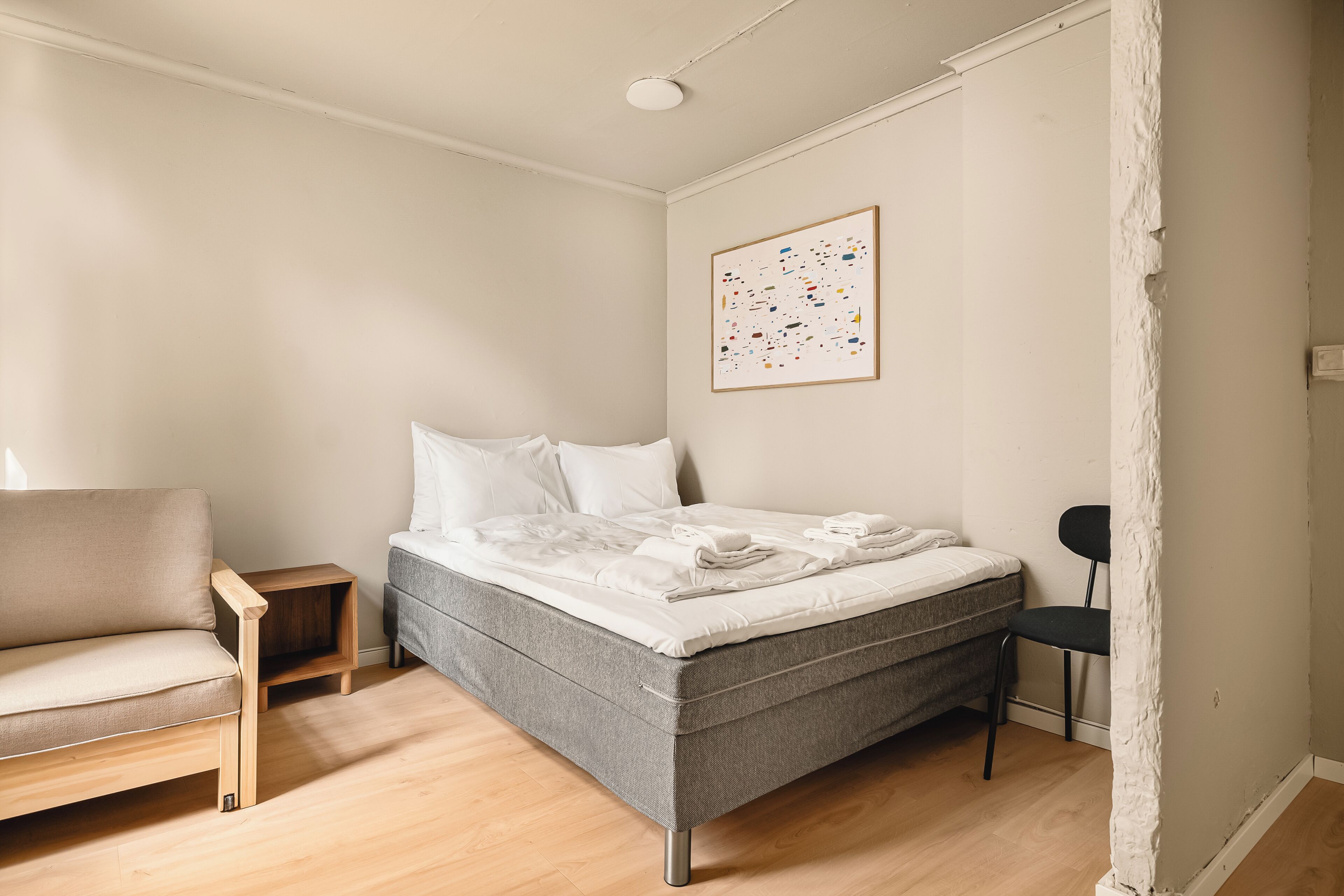 A bedroom with a bed, a chair, a small table, and a wall-mounted picture.