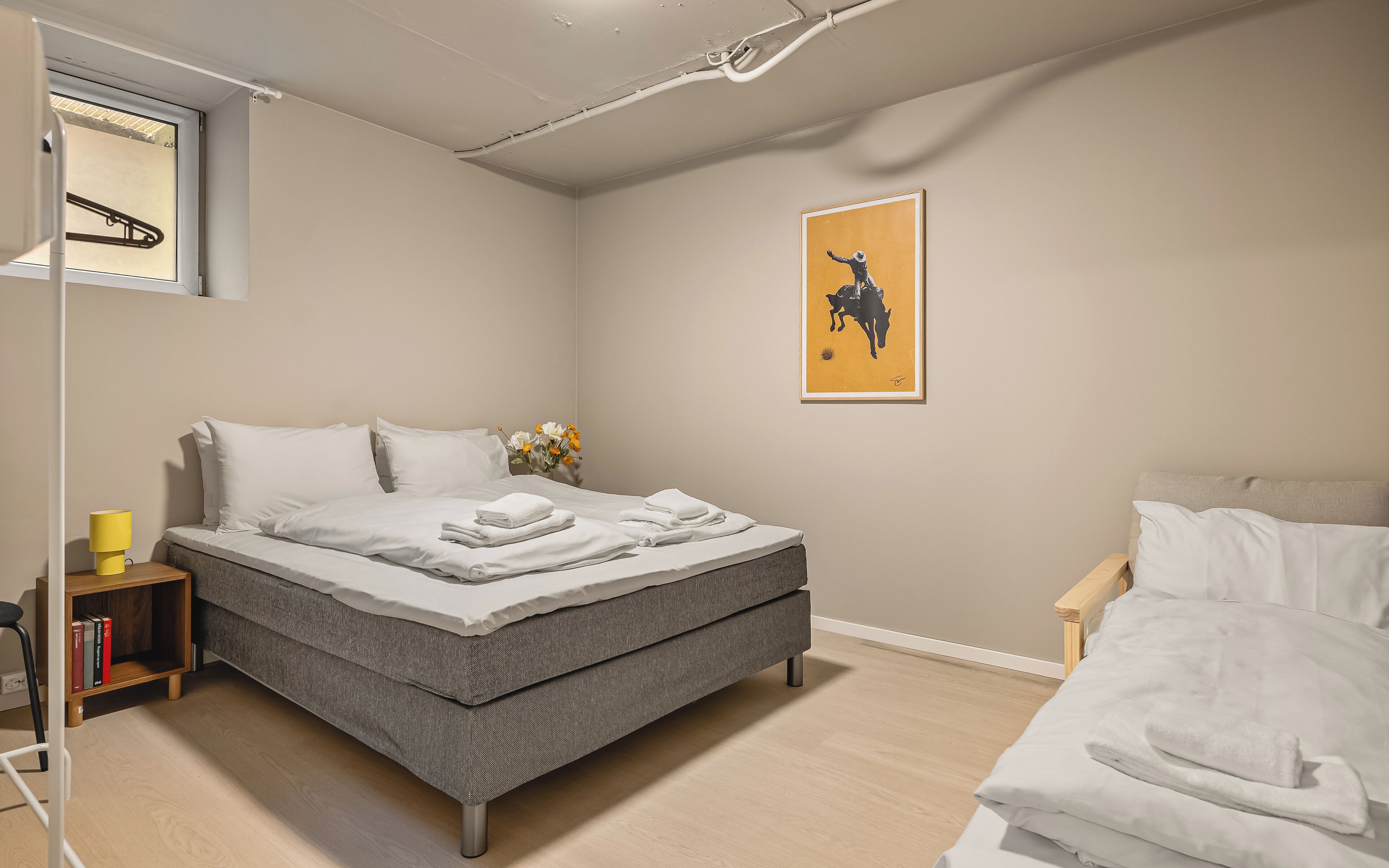 A neatly made bed with white linens, a bedside table with a lamp, and a framed artwork on the wall.
