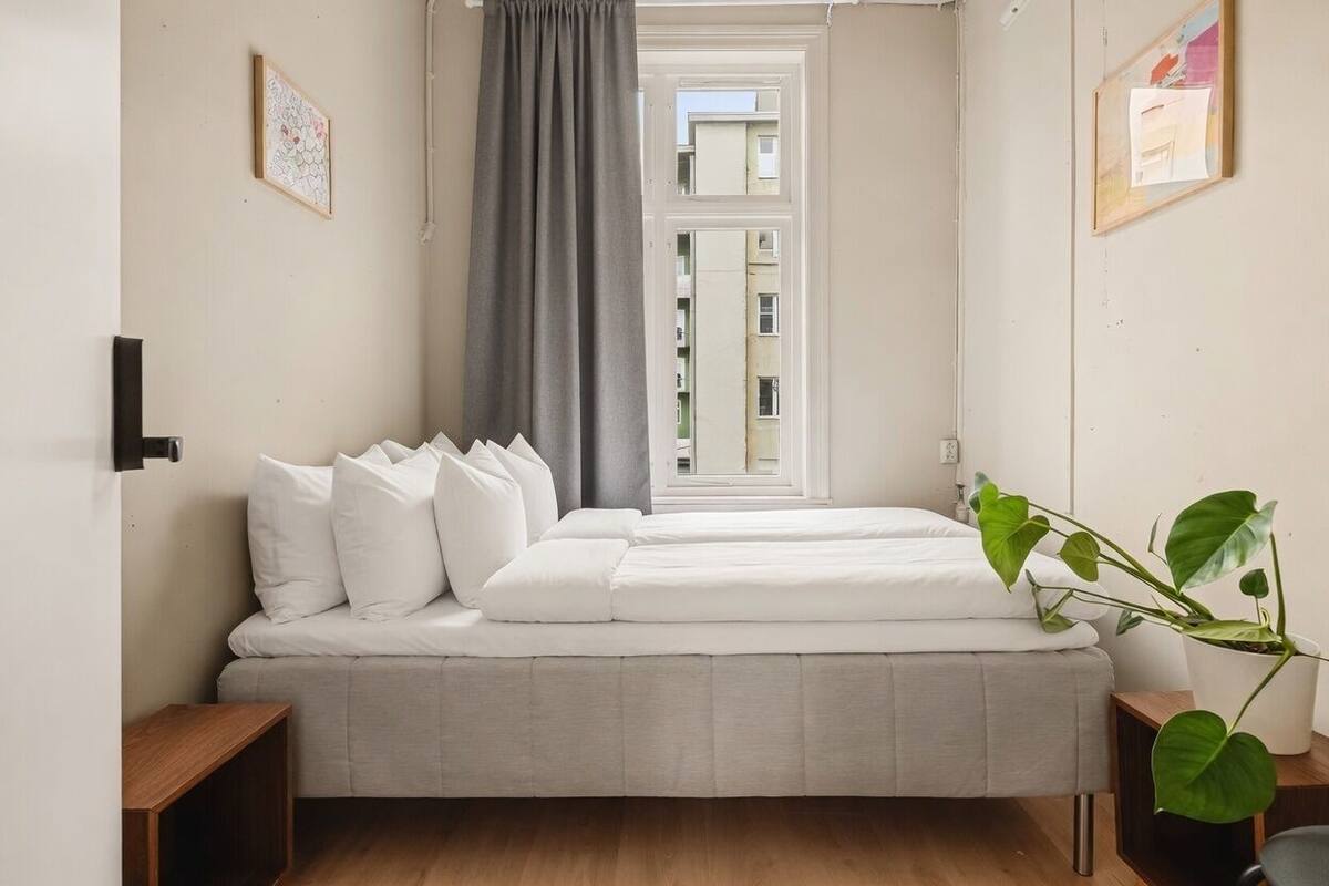 Un dormitorio con cama, ventana, planta en maceta y lámpara fijada a la pared.