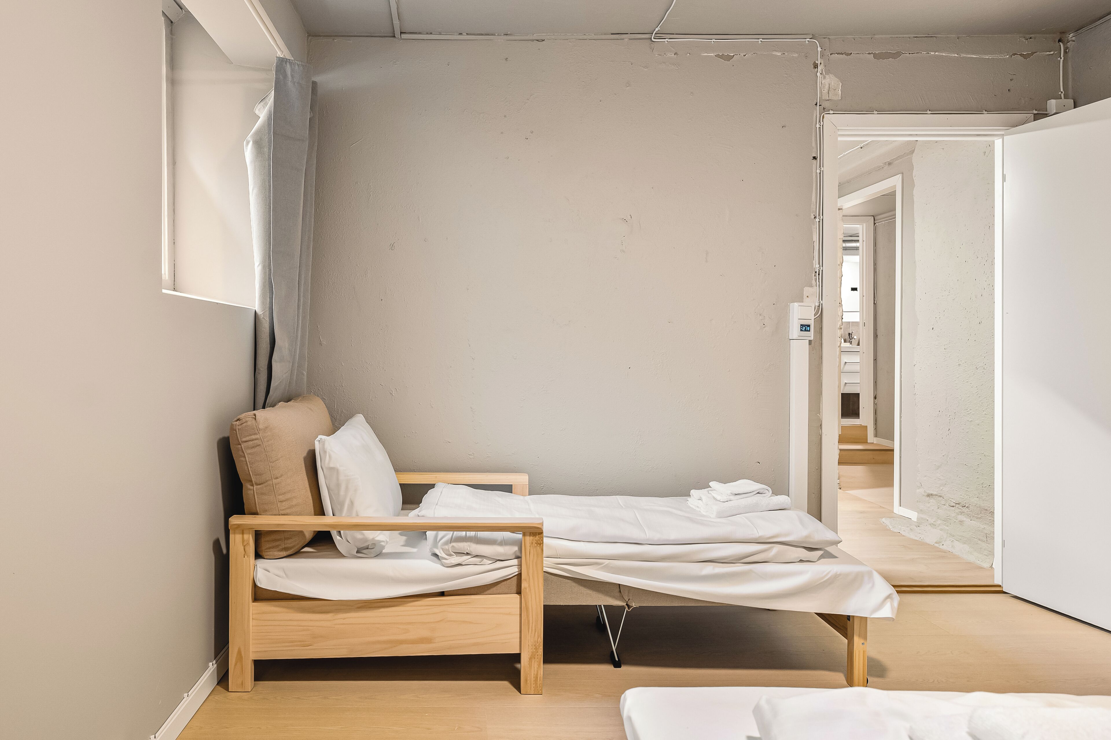A bedroom with a wooden bed, a window with a curtain, and a hallway leading to other rooms.