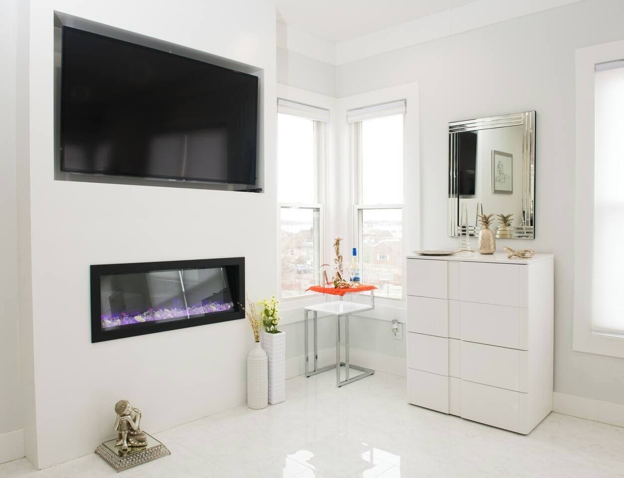Un baño moderno con un espejo grande, un tocador blanco y una chimenea.