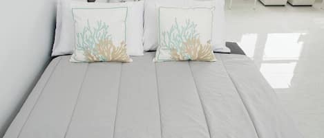 Un lit avec un matelas gris clair, deux oreillers à motifs corail et un couvre-lit bleu texturé.