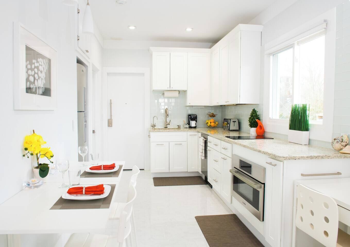 A modern kitchen with white cabinetry, a dining area with a table set for two, and a window providing natural light.