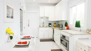 A modern kitchen with white cabinetry, a dining area with a table set for two, and a window providing natural light.