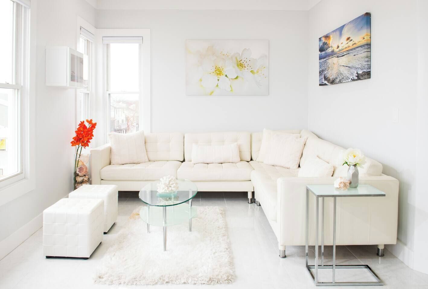 A modern living room with a white sofa, a glass coffee table, and a white rug.