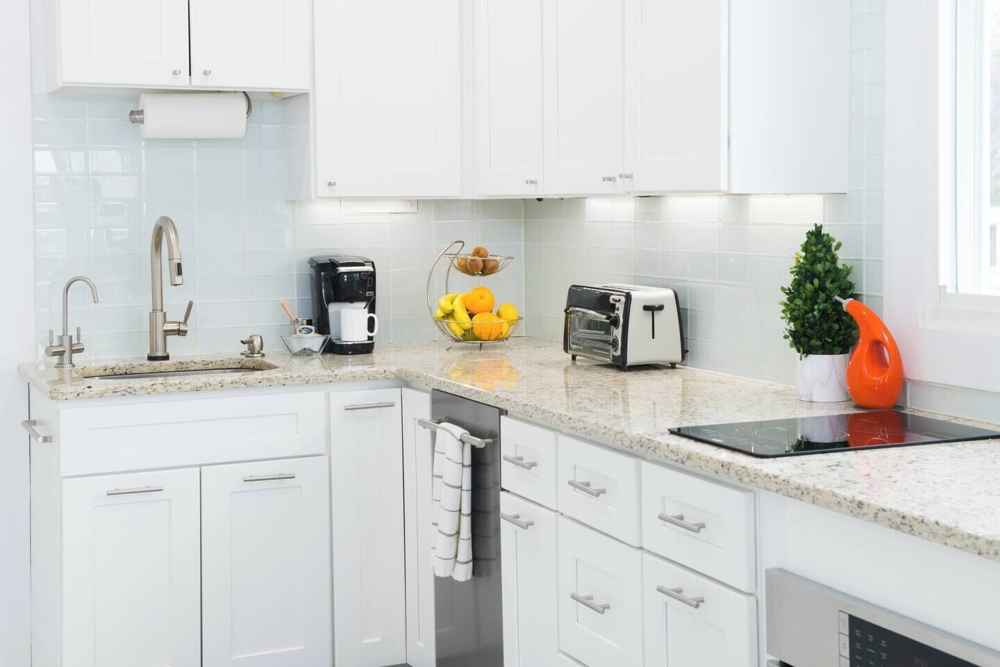 A modern kitchen with white cabinets, a stainless steel sink, a coffee maker, a toaster, and a small potted plant.
