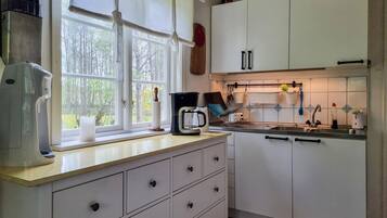 A kitchen with white cabinets, a coffee maker, and a window with a view of trees.