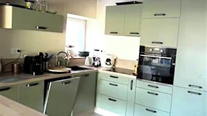 A kitchen with light green cabinets, a wooden table, and a built-in oven. - Grande Maison Familiale Chez Paulette ★ Games, Petanque & Nature (Gouzon)