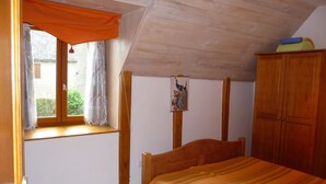 Une chambre à coucher avec un lit en bois, une fenêtre avec des rideaux, une armoire en bois et un tableau accroché au mur.