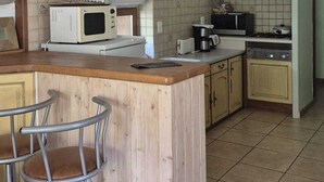 Une cuisine avec un îlot central en bois, des tabourets de bar, un four à micro-ondes, une cuisinière et des murs carrelés.