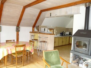 A dining area with a table and chairs, a kitchen with a stove, and a bar area. - Quiet gite on a shady plot Near the medieval town of Conques (Espeyrac)