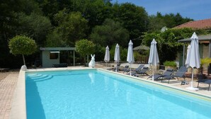 Una piscina con lettini e ombrelloni, circondata da alberi e un piccolo edificio.