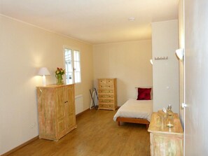 Une chambre avec une armoire en bois, un lit avec un oreiller rouge, une table de chevet avec une bouteille et une fenêtre.