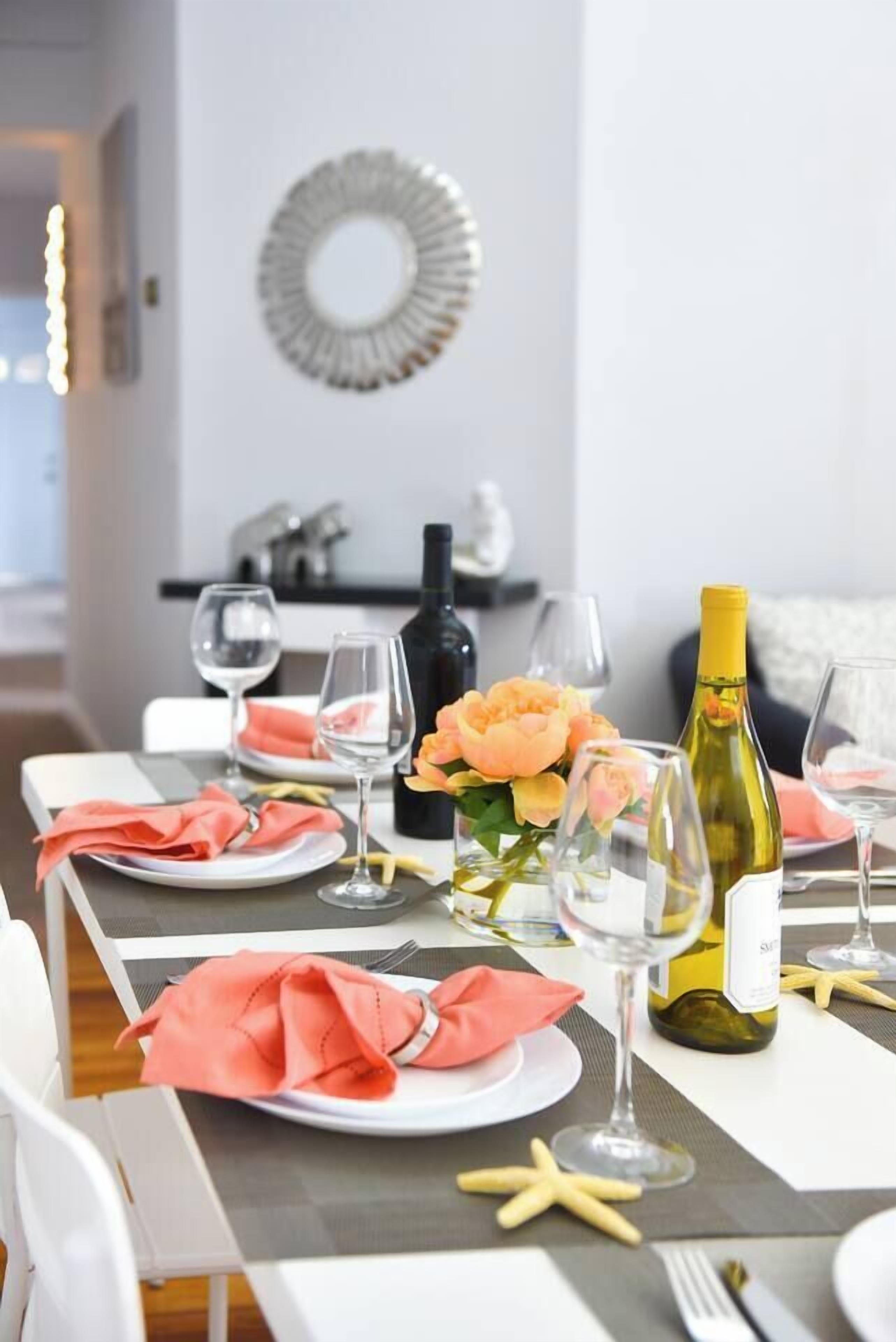 A dining table set with plates, glasses, and a bottle of wine, with a decorative mirror and a starfish on the table.