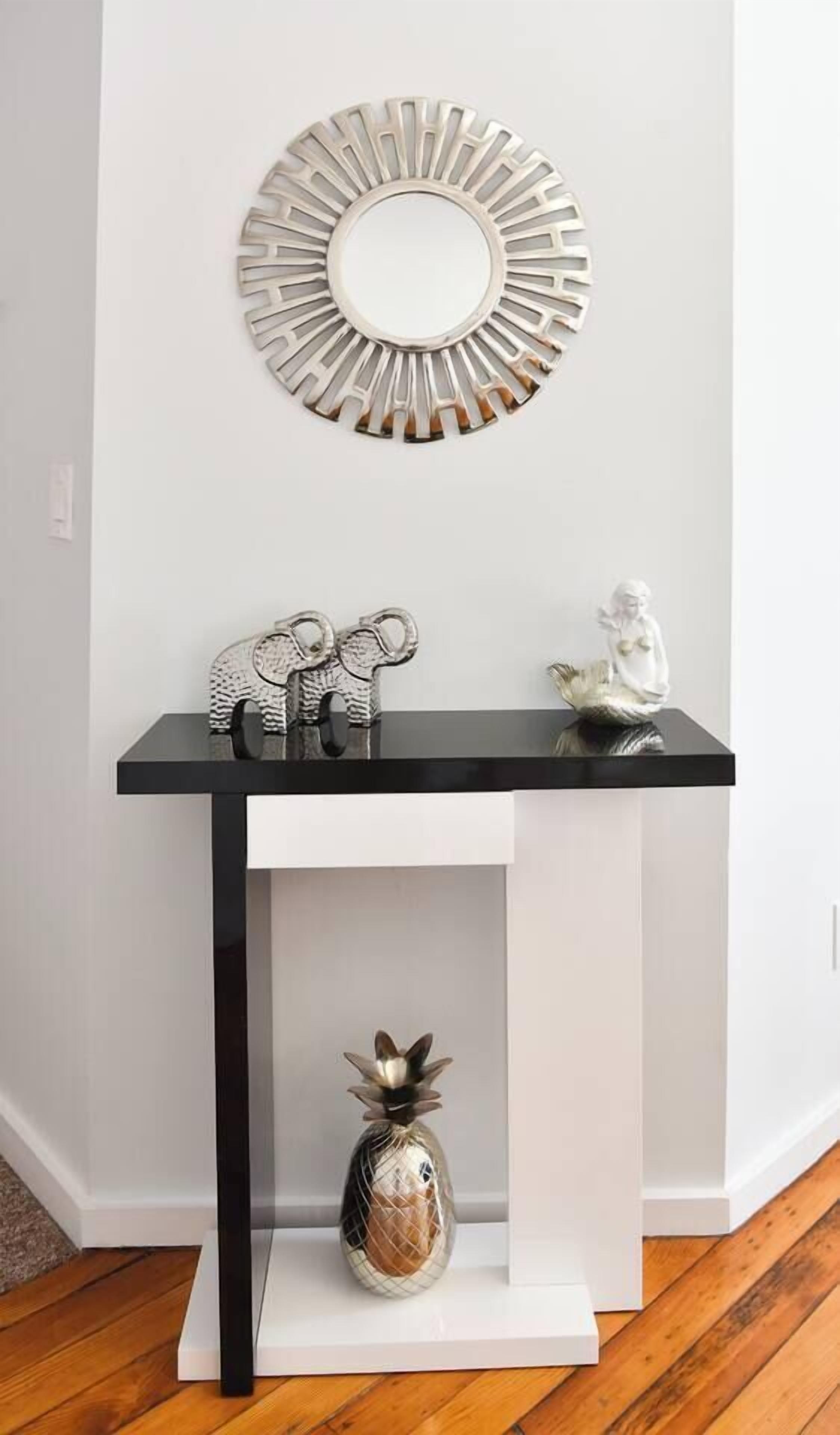 A white wall with a black console table, a decorative mirror, and two small figurines.