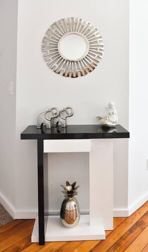 Un mur blanc orné d’une console noire, d’un miroir décoratif et de deux petites figurines.