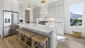 Uma cozinha moderna com armários brancos, eletrodomésticos de aço inoxidável e uma ilha grande com banquetas.