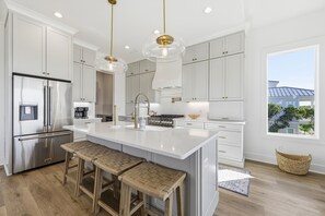 Une cuisine moderne avec des meubles blancs, des appareils en acier inoxydable et un grand îlot central doté de tabourets de bar.