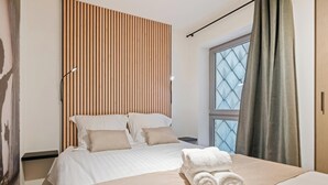 Ein Hotelzimmer mit Bett, Kopfstütze, einem Fenster mit Vorhängen und einem Handtuch auf dem Bett.