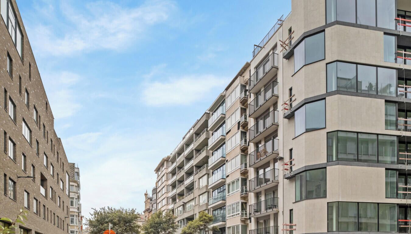 Een meerlaags woongebouw met balkons, grote ramen en een heldere lucht.