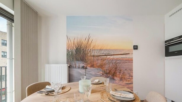 Ein Essbereich mit einem Tisch für vier Personen, einem großen Gemälde mit Strandmotiv und einem modernen Backofen an der Wand.