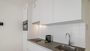 Eine moderne Küche mit weißen Schränken, einer Edelstahl-Spüle, einem eingebauten Backofen und einer Kaffeemaschine.