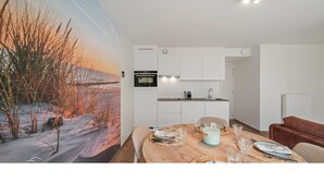 Eine moderne Küche mit weißen Schränken, einem eingebauten Backofen und einem Essbereich mit einem Holztisch, gedeckt für vier Personen.