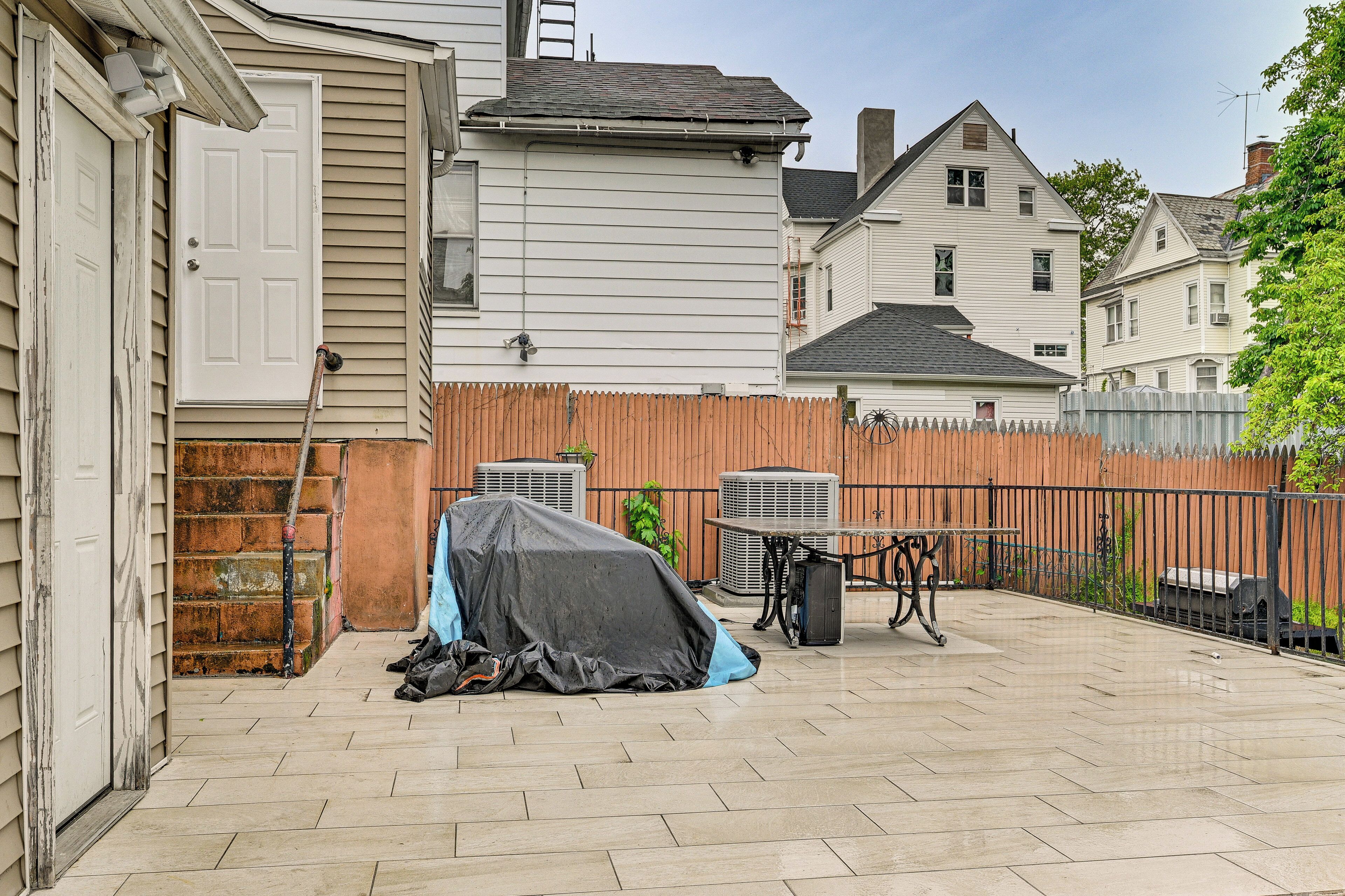 A backyard patio with a covered grill, outdoor furniture, and a wooden fence.