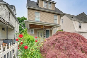 A two-story house with a front porch, a white picket fence, and a large bush with pink foliage. - Walk to the NYC Train! Mt Vernon Escape w/ Patio (Mount Vernon)