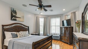 A bedroom with a wooden bed, a ceiling fan, a TV, a dresser, and a painting on the wall.
