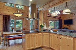 A wooden cabin interior with a kitchen, dining area, and a large window. - Beach & Dock Access! Waterfront Payette Lake Home (McCall)