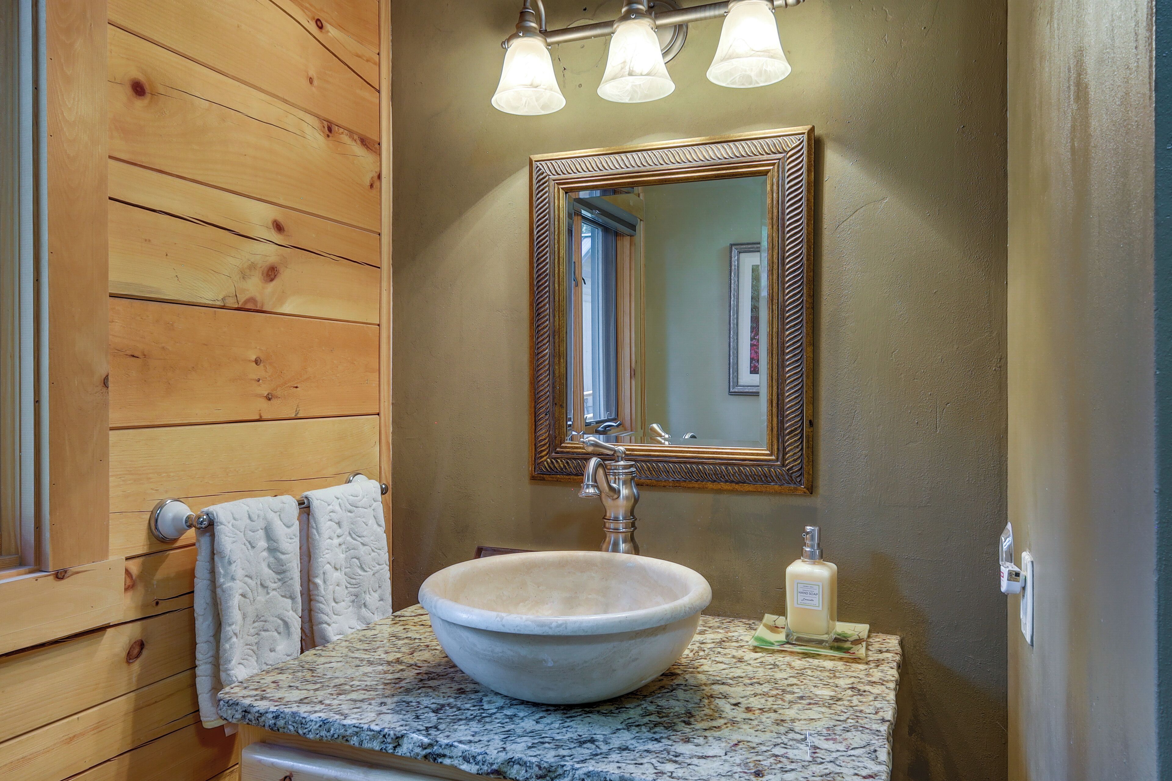 A bathroom with a wooden wall, a large vessel sink, a mirror, and a towel rack.