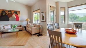 A living room with a sofa, coffee table, and dining table with chairs. There is a painting on the wall and a window with a view. - Golf, Hike & Unwind: Oro Valley Townhome w/ Patio! (Oro Valley)