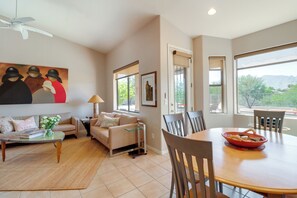 A living room with a sofa, coffee table, and dining table with chairs. There is a painting on the wall and a window with a view. - Golf, Hike & Unwind: Oro Valley Townhome w/ Patio! (Oro Valley)