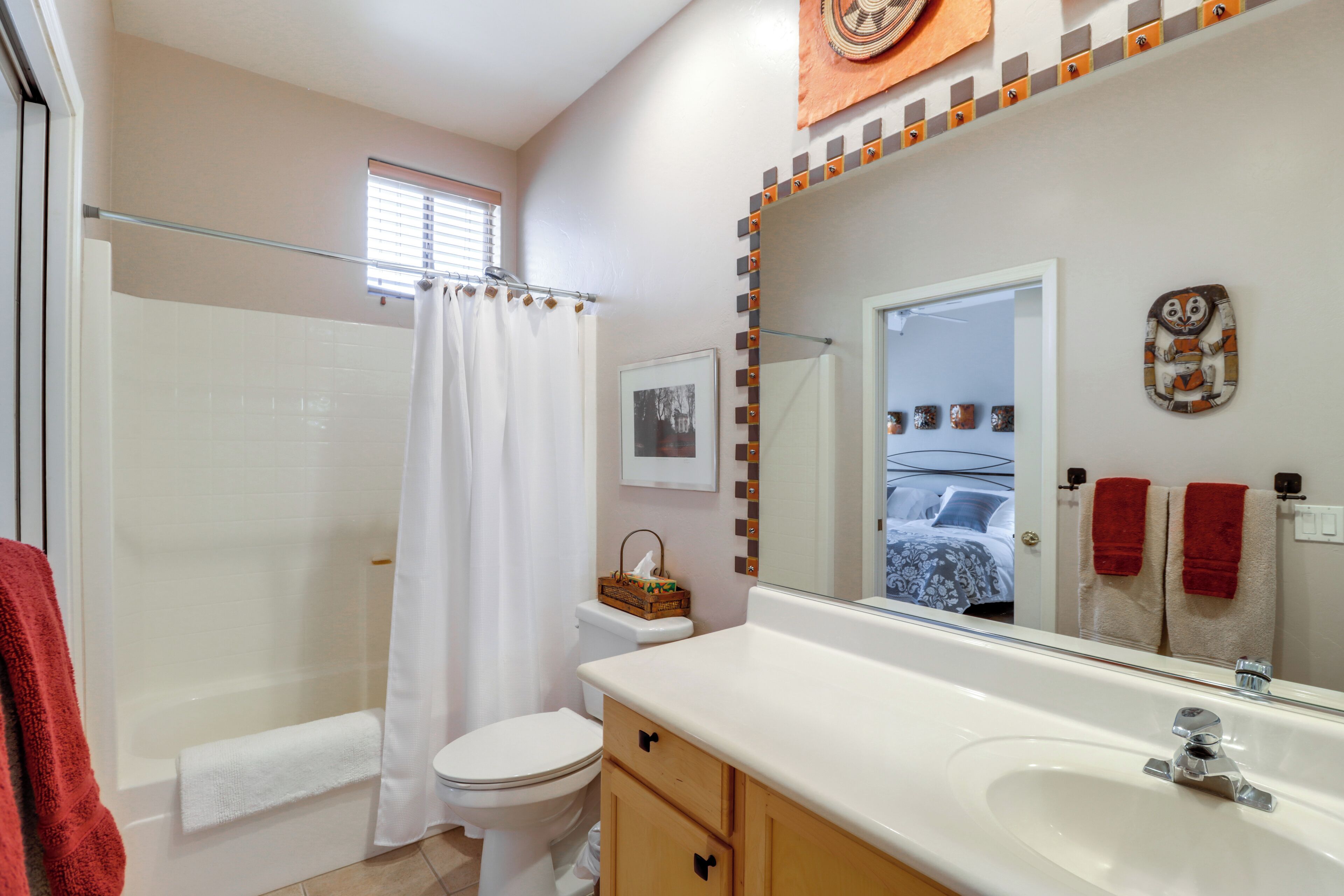 A bathroom with a shower, toilet, sink, and a mirror reflecting a bed and towels.
