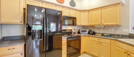 A kitchen with wooden cabinets, a stainless steel refrigerator, a microwave, and an oven.