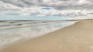 Uma praia com uma extensa faixa de areia, mar calmo e céu nublado.
